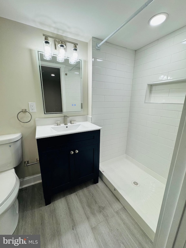 bathroom featuring wood-type flooring, a tile shower, vanity, and toilet