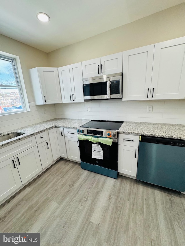 kitchen with white cabinetry, decorative backsplash, light hardwood / wood-style flooring, and appliances with stainless steel finishes