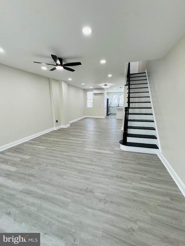 basement with a wall mounted AC, hardwood / wood-style flooring, stainless steel refrigerator, and ceiling fan