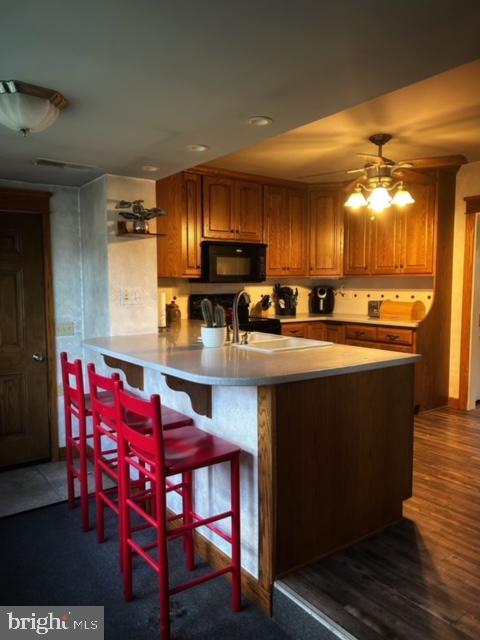 kitchen with sink, ceiling fan, hardwood / wood-style floors, a kitchen bar, and kitchen peninsula