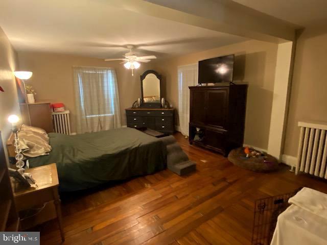 bedroom with dark hardwood / wood-style floors, radiator, and ceiling fan