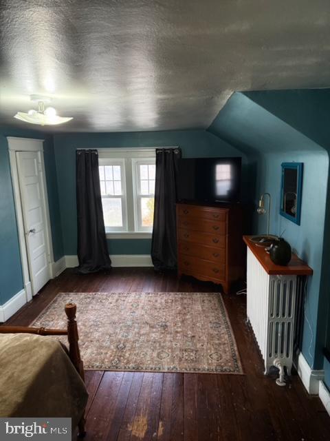 unfurnished bedroom with radiator heating unit, vaulted ceiling, dark hardwood / wood-style floors, and a textured ceiling