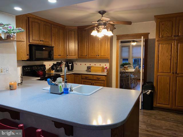 kitchen featuring a breakfast bar, black appliances, sink, dark hardwood / wood-style flooring, and kitchen peninsula