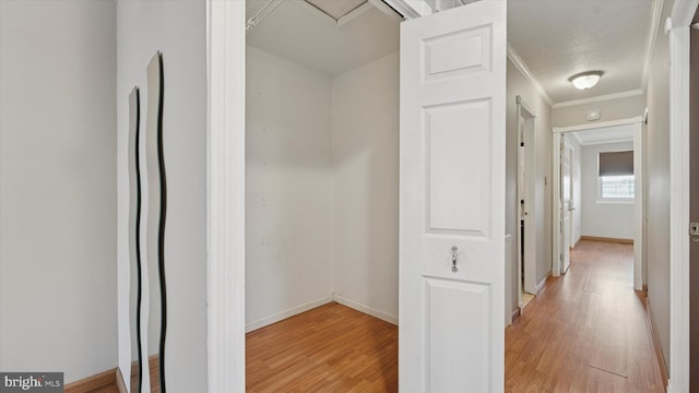 hall with light wood-type flooring, baseboards, and ornamental molding