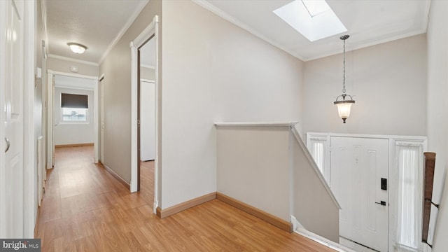 hallway featuring baseboards, a skylight, crown molding, an upstairs landing, and light wood-type flooring