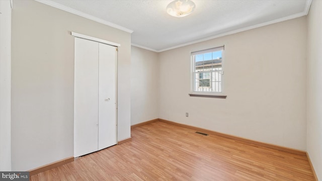 unfurnished bedroom with wood finished floors, baseboards, visible vents, ornamental molding, and a closet