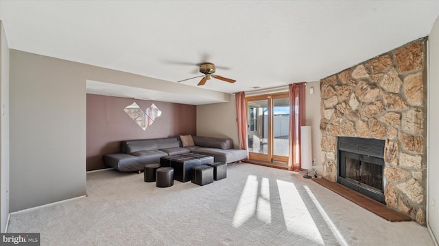 living area with a stone fireplace, carpet, and a ceiling fan