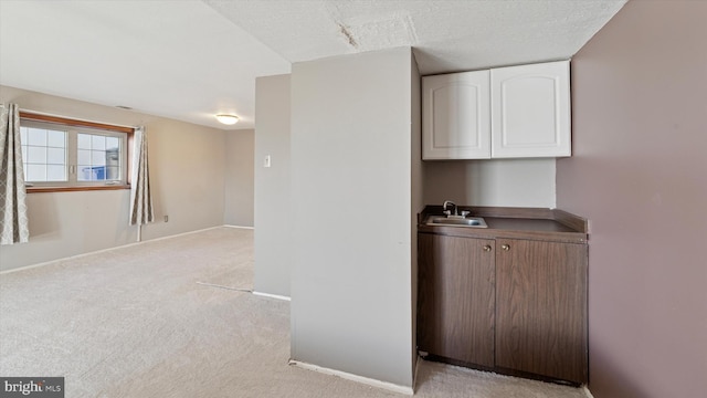 bar featuring a sink, baseboards, light colored carpet, and a textured ceiling