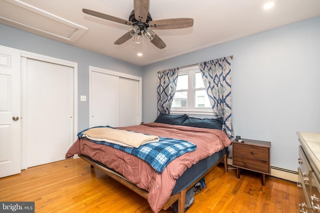 bedroom featuring a baseboard heating unit, ceiling fan, multiple closets, and light wood-type flooring