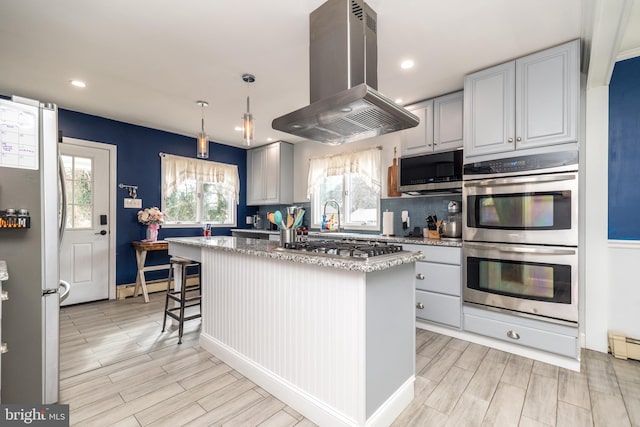 kitchen featuring appliances with stainless steel finishes, island range hood, gray cabinets, and a kitchen island