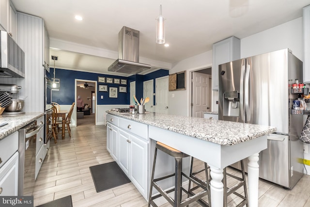 kitchen featuring a breakfast bar, island range hood, white cabinetry, hanging light fixtures, and stainless steel appliances