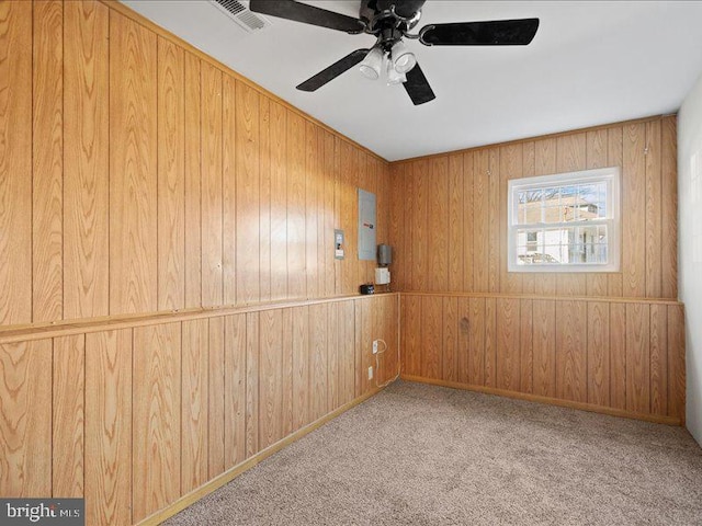 empty room featuring ceiling fan, light colored carpet, electric panel, and wood walls