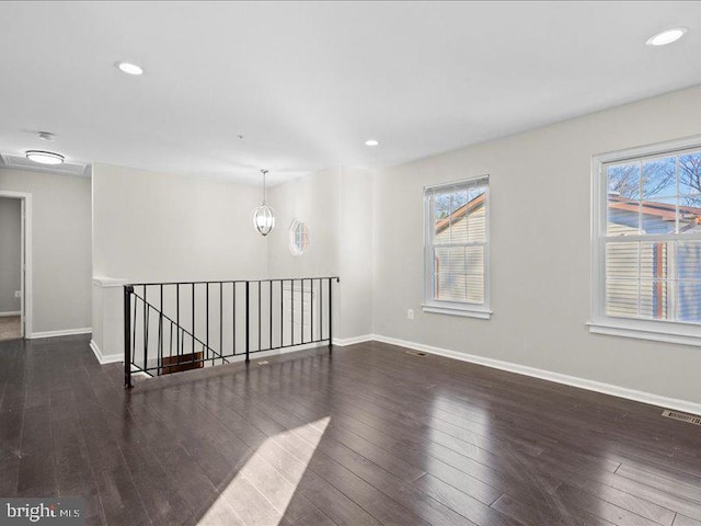 empty room with an inviting chandelier, dark wood-type flooring, and a healthy amount of sunlight