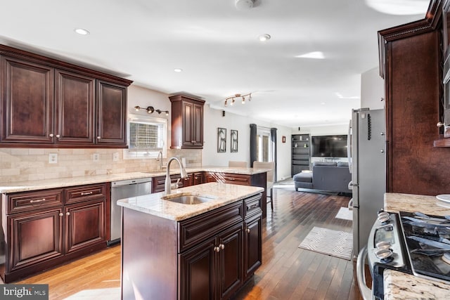 kitchen with backsplash, hardwood / wood-style flooring, stainless steel appliances, and a center island with sink