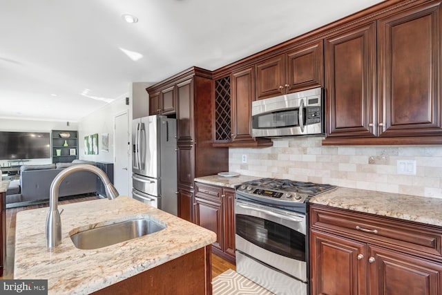 kitchen with light stone countertops, appliances with stainless steel finishes, sink, and decorative backsplash