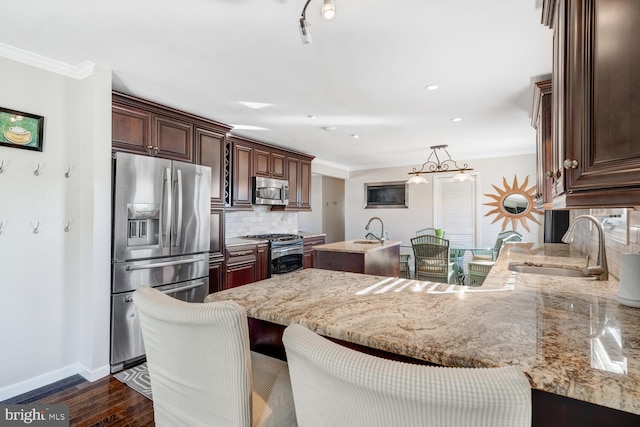 kitchen featuring dark wood-type flooring, hanging light fixtures, ornamental molding, appliances with stainless steel finishes, and backsplash