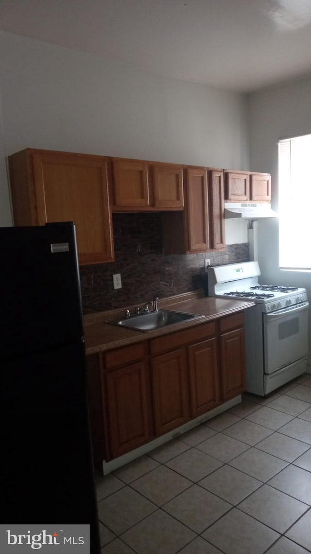 kitchen featuring light tile patterned flooring, sink, tasteful backsplash, black refrigerator, and white gas range