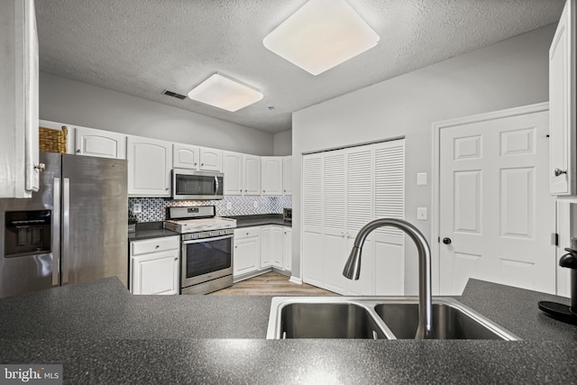 kitchen with sink, appliances with stainless steel finishes, tasteful backsplash, a textured ceiling, and white cabinets