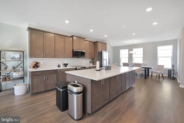 kitchen with pendant lighting, dark wood-type flooring, an island with sink, and appliances with stainless steel finishes