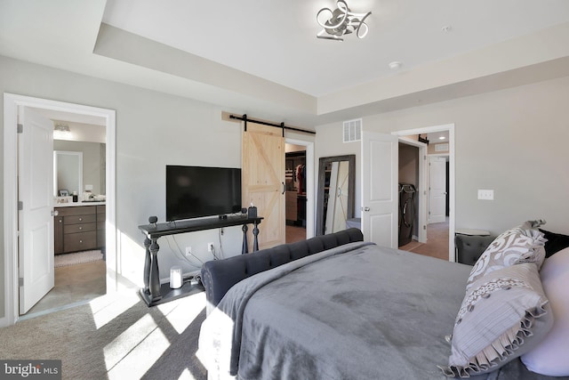 carpeted bedroom with ensuite bath, a barn door, a raised ceiling, and a spacious closet