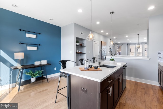 kitchen featuring hanging light fixtures, an island with sink, sink, and a breakfast bar