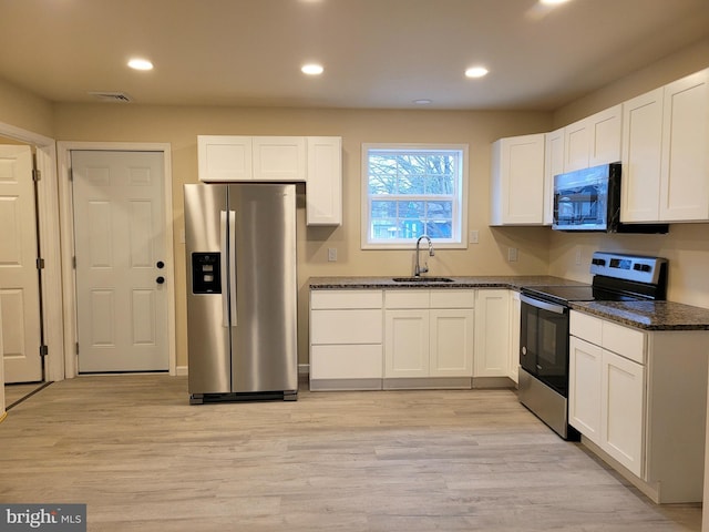 kitchen with appliances with stainless steel finishes, sink, dark stone countertops, white cabinets, and light hardwood / wood-style flooring