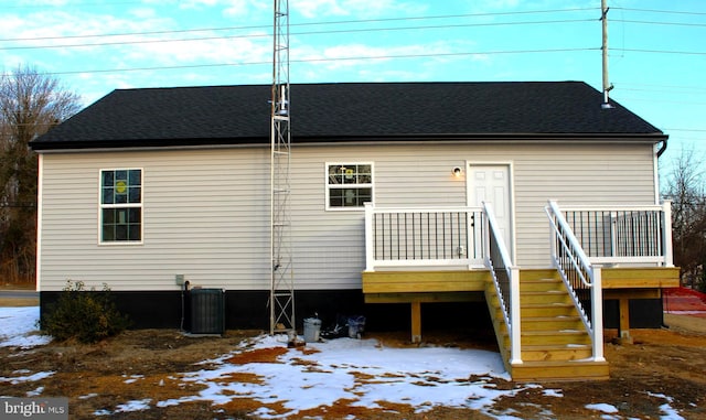 snow covered rear of property featuring central AC unit