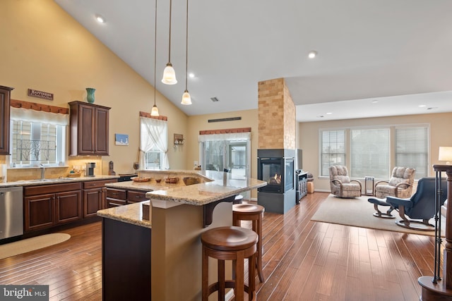 kitchen with open floor plan, a large island with sink, a kitchen breakfast bar, dark wood-style floors, and stainless steel dishwasher