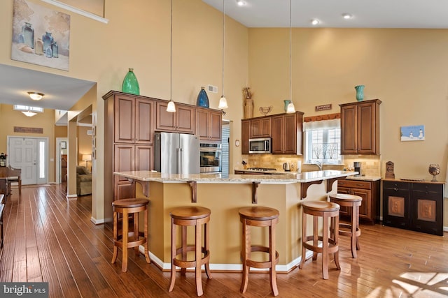 kitchen with light stone countertops, light wood finished floors, a breakfast bar, stainless steel appliances, and tasteful backsplash