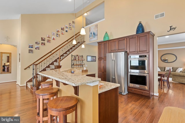 kitchen featuring light stone counters, visible vents, dark wood finished floors, a towering ceiling, and appliances with stainless steel finishes