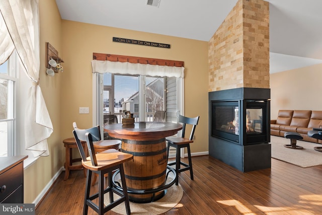 dining space with visible vents, dark wood-type flooring, lofted ceiling, baseboards, and a multi sided fireplace