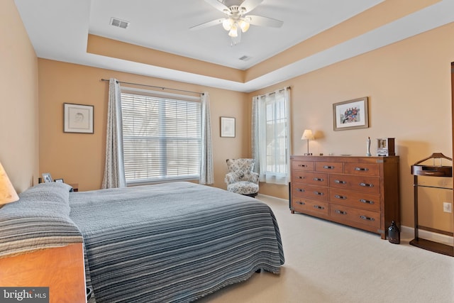 carpeted bedroom with visible vents, baseboards, a tray ceiling, and a ceiling fan