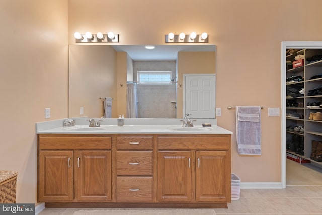 bathroom with a walk in closet, double vanity, a tile shower, and a sink