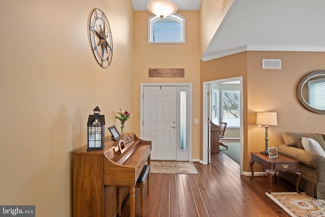 foyer with dark wood finished floors, a high ceiling, baseboards, and visible vents