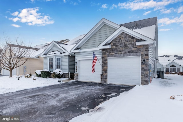 view of front facade with aphalt driveway, central air condition unit, an attached garage, and stone siding