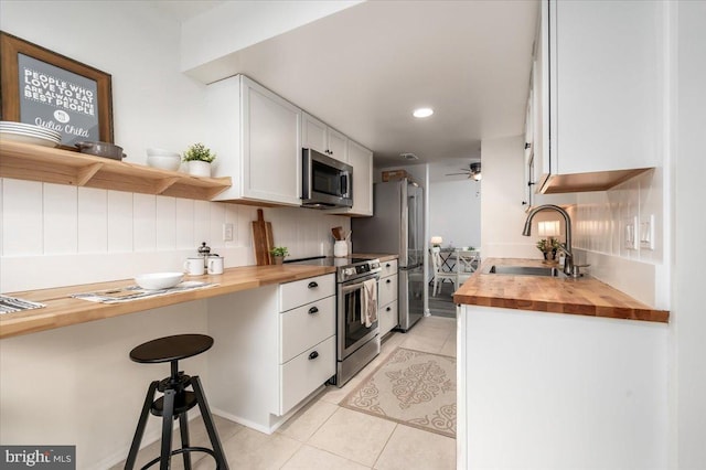 kitchen featuring light tile patterned flooring, butcher block counters, sink, appliances with stainless steel finishes, and white cabinets