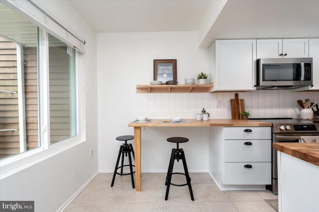 kitchen featuring appliances with stainless steel finishes, tasteful backsplash, butcher block counters, white cabinets, and light tile patterned floors