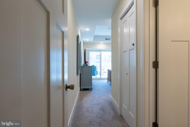 hall featuring light carpet and a tray ceiling