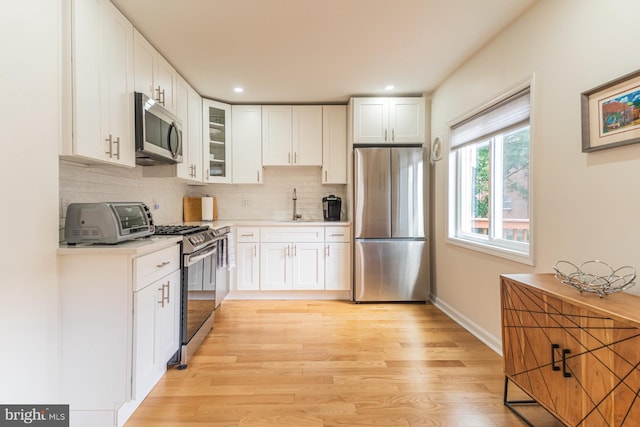 kitchen featuring sink, backsplash, stainless steel appliances, white cabinets, and light wood-type flooring