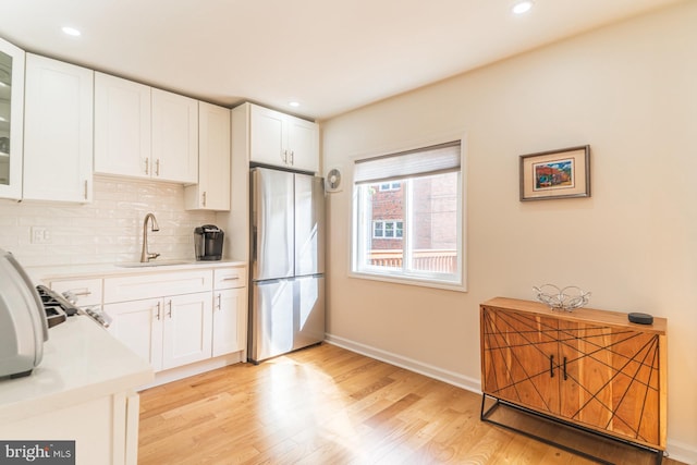 kitchen featuring sink, stainless steel fridge, white cabinetry, light hardwood / wood-style floors, and decorative backsplash