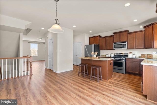 kitchen with a center island, appliances with stainless steel finishes, a kitchen breakfast bar, pendant lighting, and light stone countertops