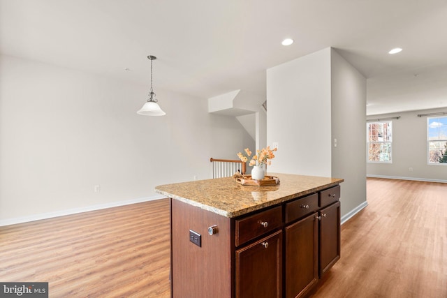 kitchen featuring a kitchen island, light stone counters, light wood-type flooring, and decorative light fixtures