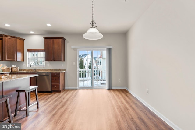 kitchen with dishwasher, light hardwood / wood-style floors, light stone counters, and decorative light fixtures