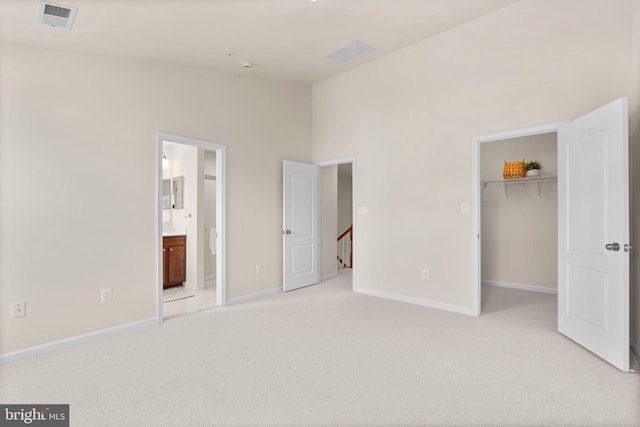 unfurnished bedroom with connected bathroom, a high ceiling, a walk in closet, light carpet, and a closet