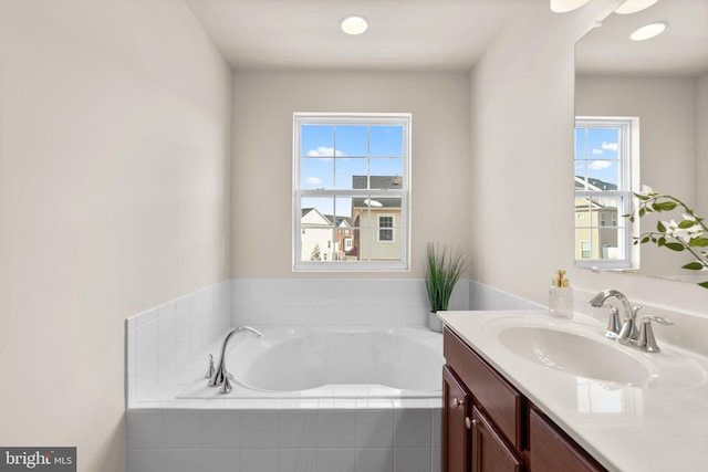 bathroom with plenty of natural light, tiled bath, and vanity