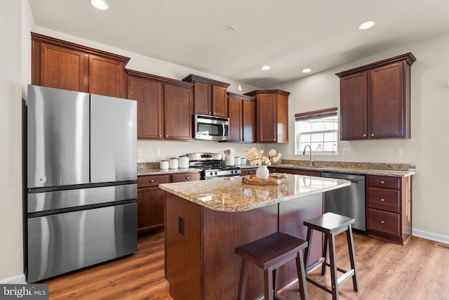 kitchen with light stone counters, a center island, a kitchen breakfast bar, hardwood / wood-style flooring, and stainless steel appliances