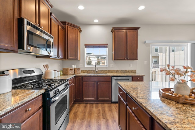 kitchen featuring appliances with stainless steel finishes, a wealth of natural light, wood-type flooring, sink, and light stone countertops