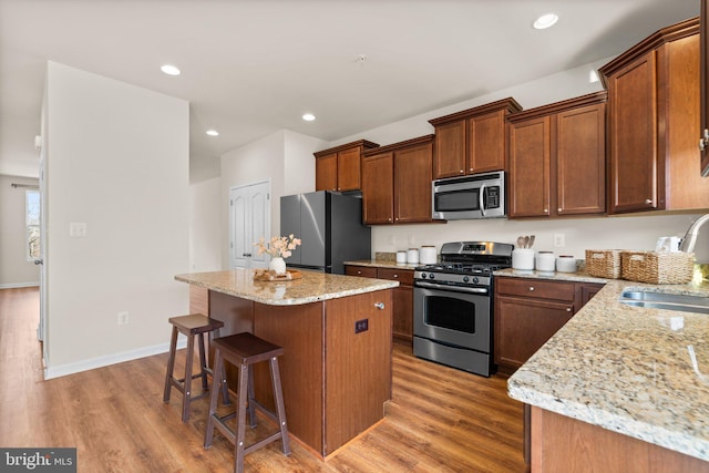 kitchen featuring stainless steel appliances, light stone countertops, a kitchen island, and sink