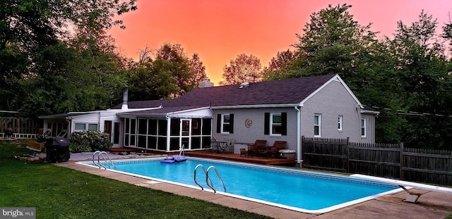 pool at dusk featuring a diving board, a yard, a patio area, and a sunroom