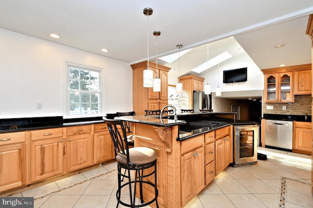 kitchen with light tile patterned flooring, a breakfast bar, appliances with stainless steel finishes, an island with sink, and beverage cooler